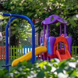 Giardino giochi colorato con altalena, scivoli e recinzione tra gli alberi.