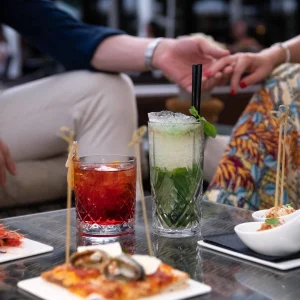 Due persone si tengono per mano a un tavolo con drink e stuzzichini.