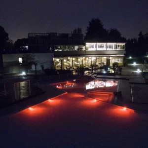 Vista notturna di una piscina illuminata di rosso davanti a un edificio moderno.