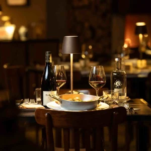 Tavolo da pranzo elegante con bottiglia di vino, bicchieri, piatto di pasta e lampada.