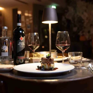 Cena elegante con piatto gourmet, vino rosso e atmosfera soffusa in un ristorante.