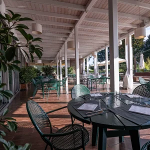 Terrazza di un ristorante con tavoli apparecchiati e sedie verdi sotto una copertura.